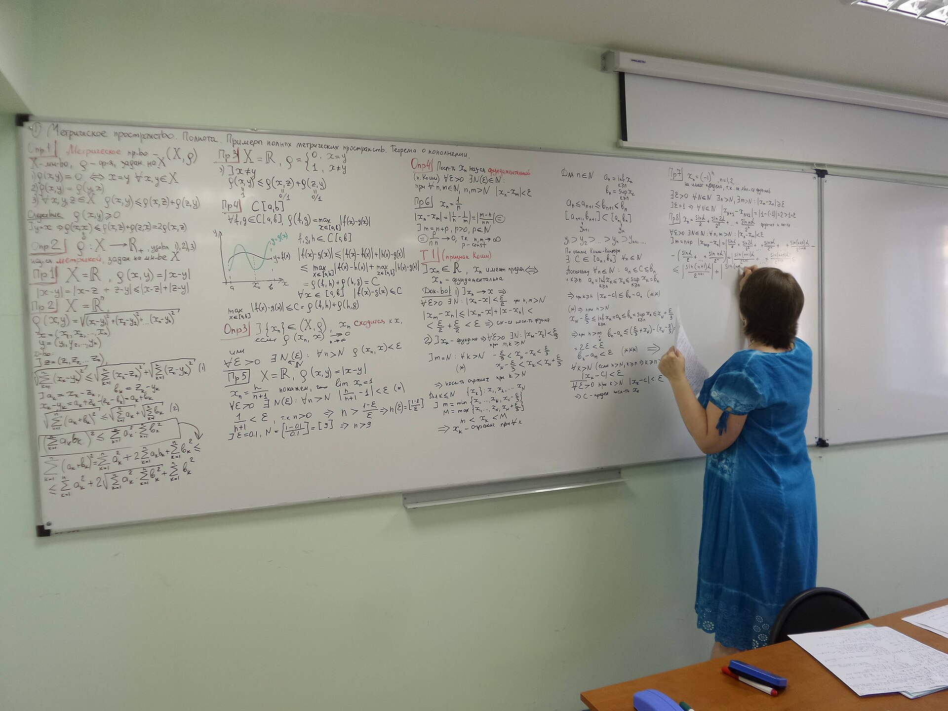 A hand writing mathematical formulas on a blackboard.